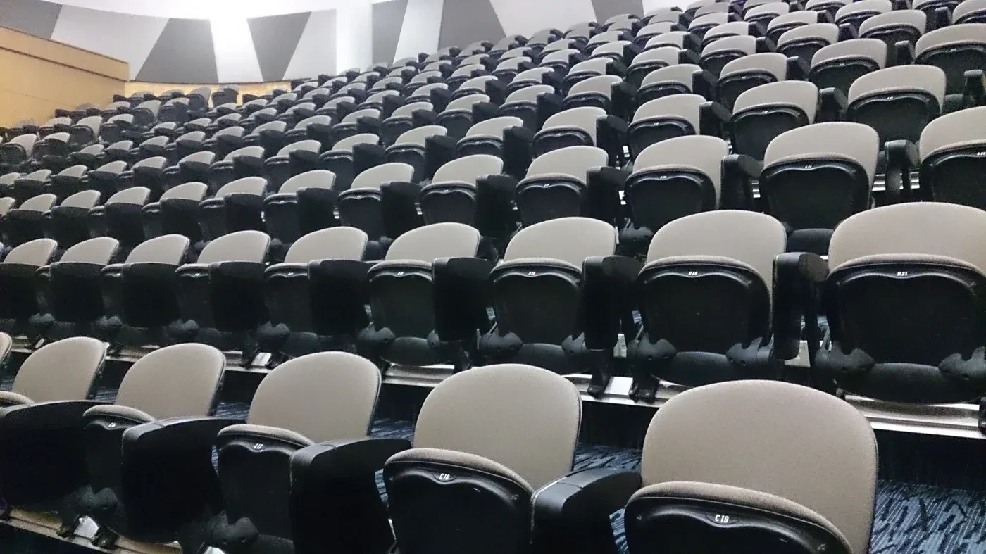 Perspectiva ampla de auditório com fileiras de assentos e piso de carpete
